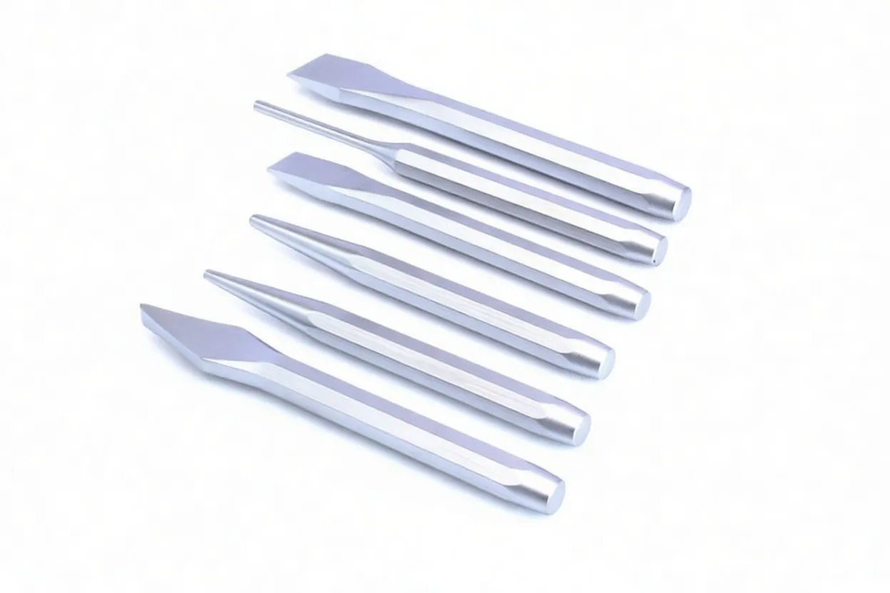 Six loose silver chisels and punches with hexagonal shanks and varied tips laid out on white background