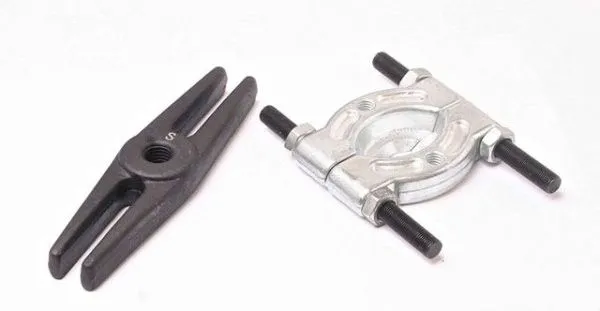 Close-up of black two-prong puller yoke marked 'S' and silver two-piece bearing splitter with threaded studs and nuts