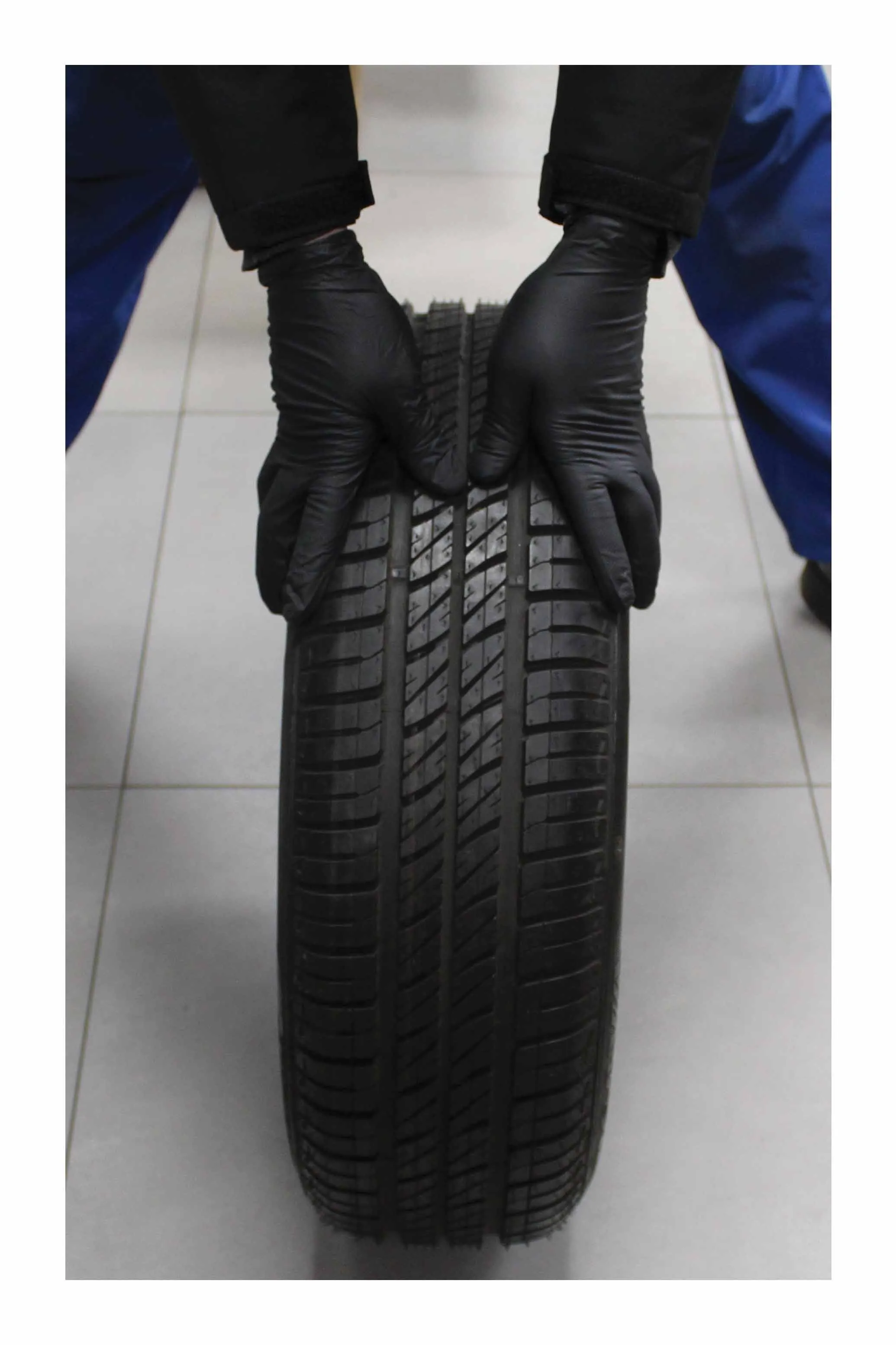 Person wearing black nitrile gloves holding a tire by the tread, showing grip and fit.
