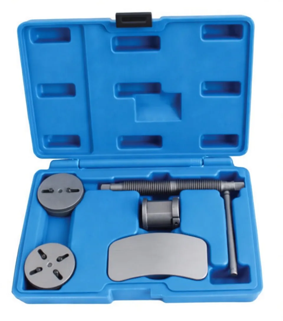 Top view of an open blue tool case containing a brake caliper piston rewind kit: two slotted round adapters, threaded T-handle screw, cylindrical adapter, and curved clamp plate with raised markings.