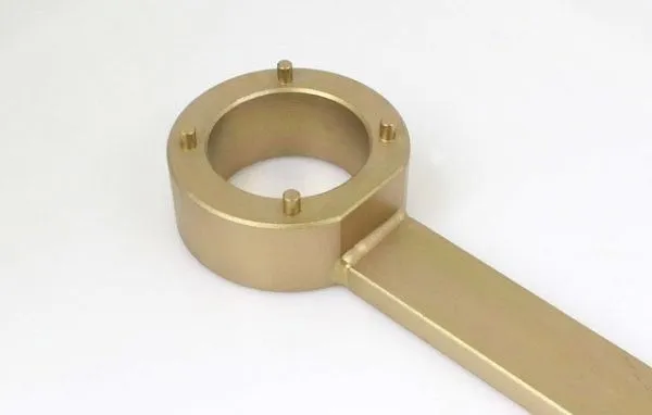 Close-up of the collar end of a gold-plated crank hold tool showing inner bore, four locator pins and welded rectangular arm.