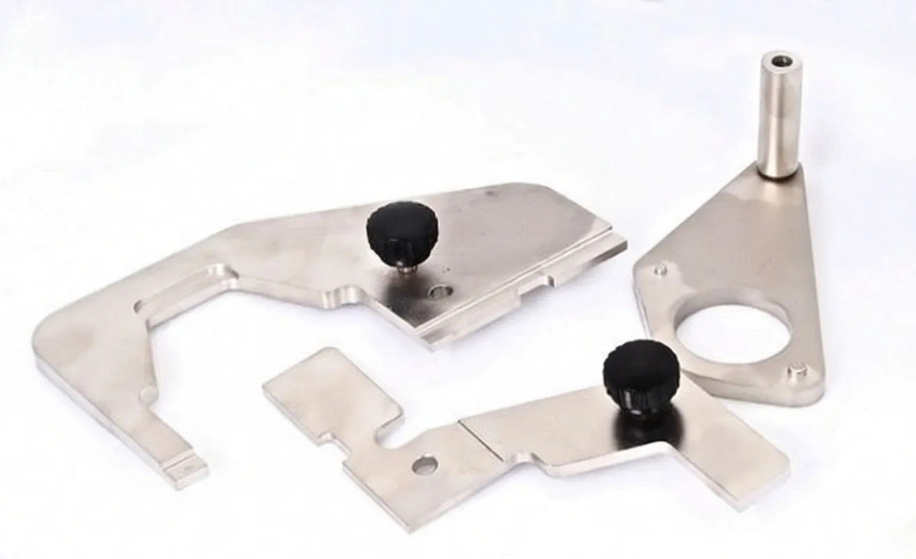 Close-up of three stainless engine timing tools: two plates with thumbscrews and a triangular locating plate with dowel pin, all stamped 'saTra'