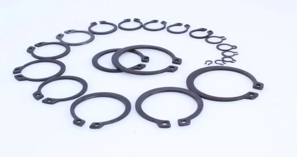 Various sizes of black external snap rings arranged on a white surface, showing open c-shapes and plier ears