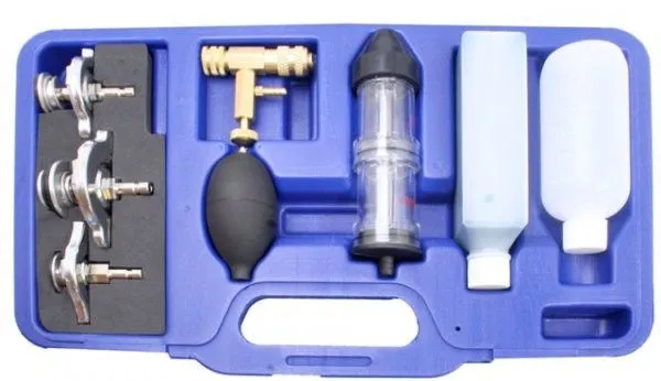 Top view of radiator pressure/vacuum tester kit in blue molded case with metal adapters, brass valve and black bulb, clear cylinder and two bottles