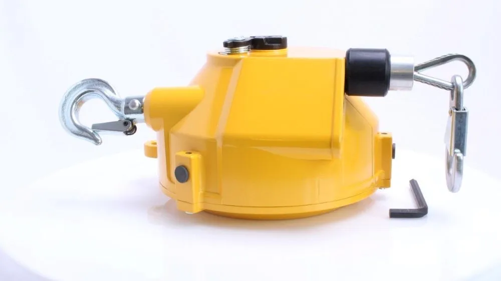 Side view of yellow spiral spring balancer showing swivel hook, cable outlet with rubber bumper and an Allen key on white surface