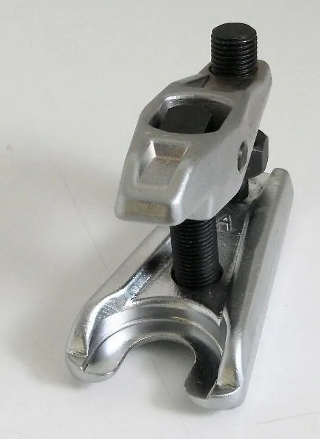 Angled view of universal ball joint extractor showing curved U-fork, central threaded rod with square/hex recess and side hex nut on clamping bolt.